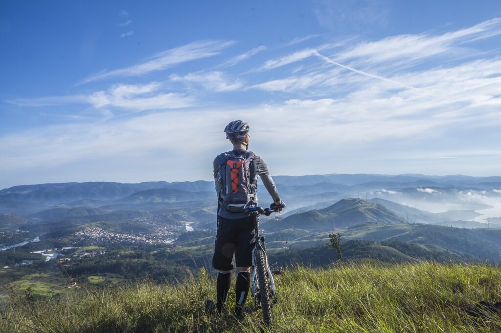 Séjour de groupe cyclotourisme dans le Vercors Trièves en Isère avec l'association AVT. Un cycliste à l'arrêt près de son vélo admire le paysage et la vue sur les montagnes.