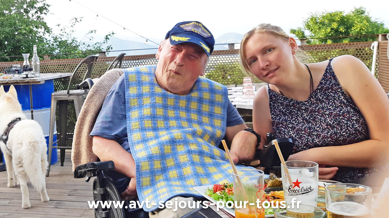 Un homme en fauteuil roulant et son accompagnatrice lors d'une sortie au restaurant. Séjour de vacances adaptées organisé par l'association AVT séjours pour tous.