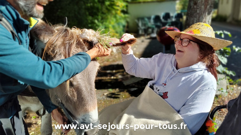 Une femme avec déficience intellectuelle caresse un âne en souriant lors d'un atelier de médiation animale. Activité adaptée proposée lors d'un séjour adapté handicap organisé par AVT séjours pour tous dans le Vercors Trièves.