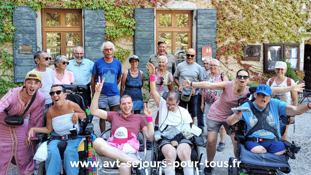 Un groupe de vacanciers en situation de handicap moteur avec leurs accompagnateurs devant le centre de vacances AVT séjours pour tous dans le Vercors Trièves. Ils sont très heureux de leurs vacances.