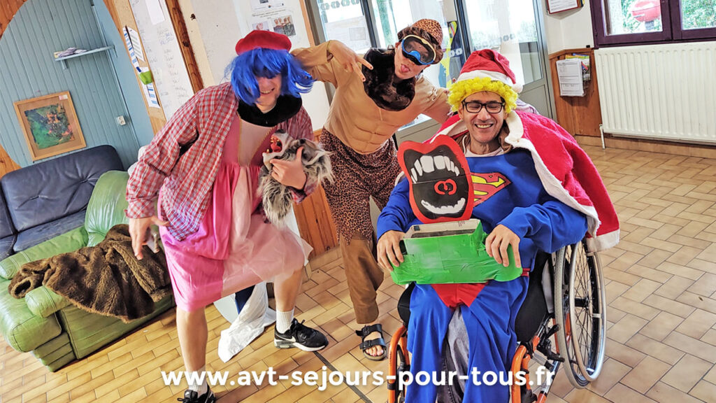 Un vacancier en fauteuil roulant est déguisé en Superman. Il est pris en photo avec deux animateurs lors d'un séjour adapté PMR organisé par AVT séjours pour tous dans le Vercors Trièves.
